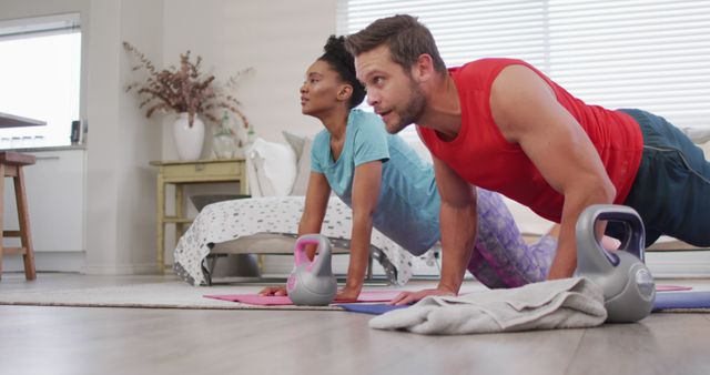Image of happy diverse couple training together at home, doing push ups. Love, relationship and spending quality time together at home.