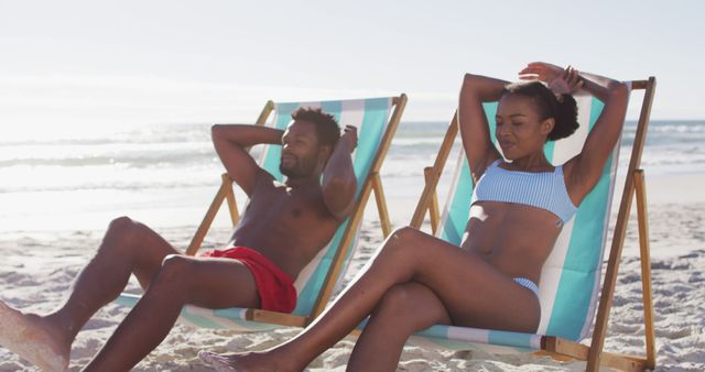 African american couple sunbathing while sitting on deck chairs at the beach. travel romantic vacation lifestyle concept