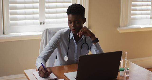 Doctor Writing Notes at Desk with Laptop and Medical Equipment - Download Free Stock Images Pikwizard.com