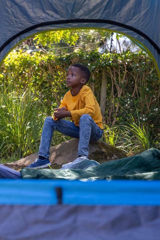 African american boy sitting at tent doorway wearing mustard shirt backyard camping