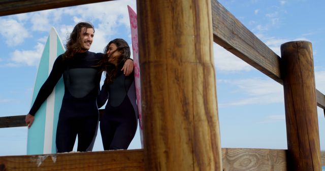 Couple in Wetsuits Holding Surfboards on Wooden Walkway at Beach - Download Free Stock Images Pikwizard.com