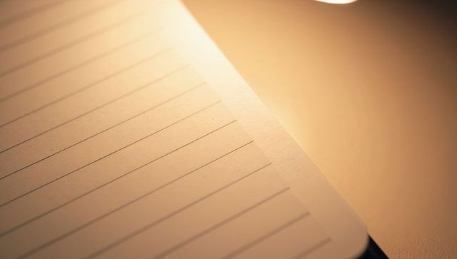 Warm lamp light catching lined notebook page, highlighting ruled margin for cozy writing workspace