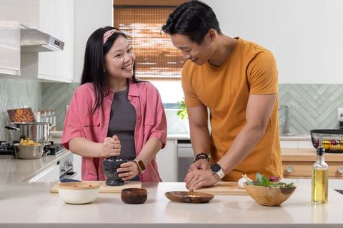 Asian couple cooking together in modern bright kitchen, smiling and preparing fresh meal