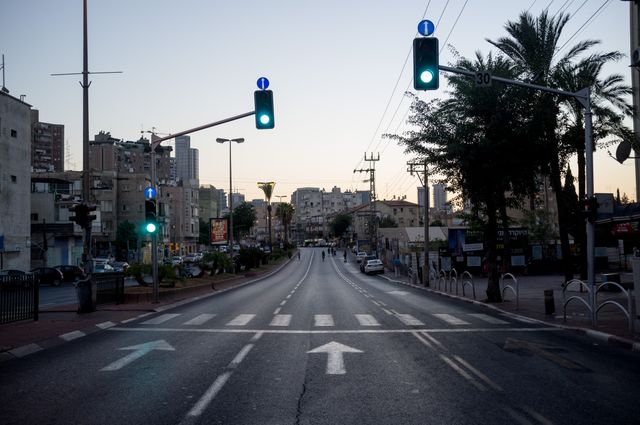 Shows empty urban road with green traffic lights early morning. Ideal for depicting urban life, transportation scenarios, quiet city moments, or introducing scenes in a story.