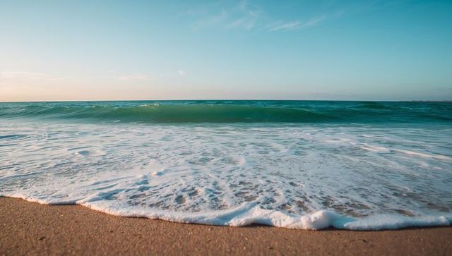 Turquoise Wave Lapping Sandy Shoreline During Golden Hour Foamy Surf Tranquil Coast