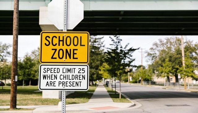 School zone speed limit sign on pole next to sidewalk curb ramp under overpass urban safety