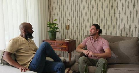 Two men enjoying relaxed conversation on sofa in modern lounge with plants and drinks