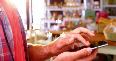 Tapping smartphone with floating thumbs-up icons on warm backlit retail counter