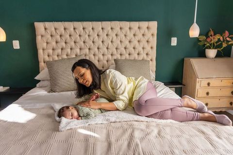 Mother bonding with sleeping newborn on sunlit tufted king bed