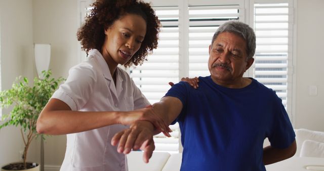 Biracial female physiotherapist helping senior man stretching his arm. senior healthcare medical home visit.