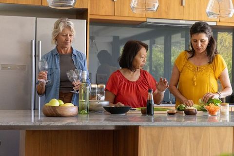 Multigenerational friends preparing dinner and pouring wine at modern kitchen island
