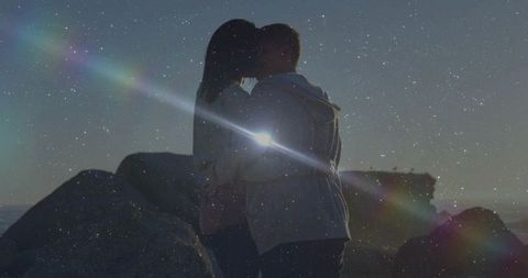 Kissing couple standing on rocky shore at sunset with lens flare silhouette romance
