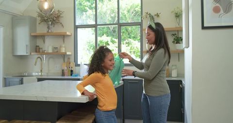 Mother handing clean cloth to smiling daughter in bright modern farmhouse kitchen