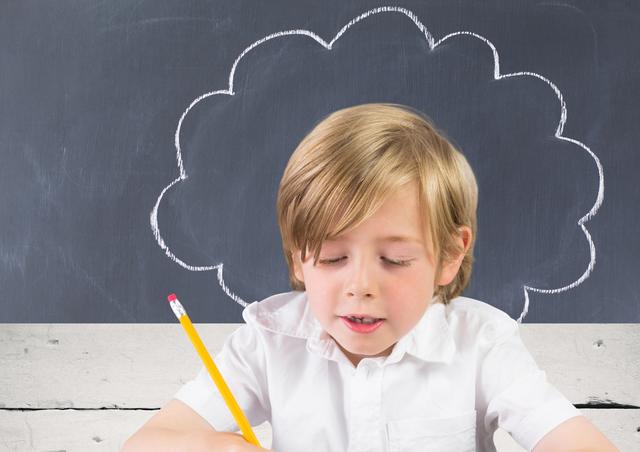 Young boy concentrating on his homework while holding a pencil, with a chalkboard in the background. Ideal for educational content, school promotions, learning materials, and child development articles.