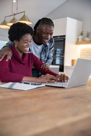 Happy couple collaborating on laptop at home kitchen