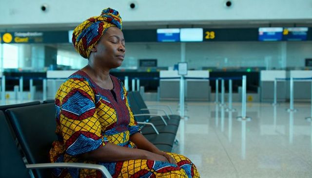 Woman resting in vibrant patterned dress and headwrap while waiting at airport gate