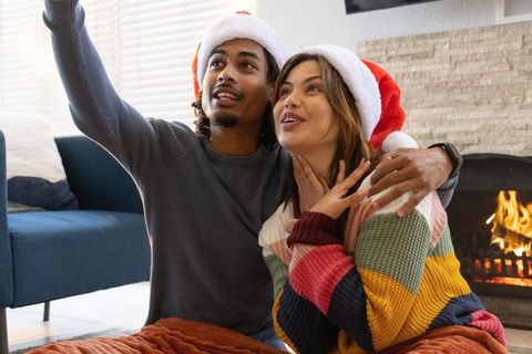 Couple wearing santa hats cuddling by fireplace taking selfie on cozy christmas morning