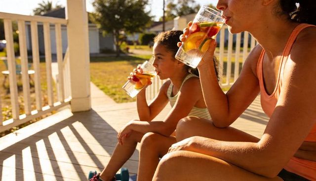 Mother and daughter relaxing on sunlit porch drinking citrus-infused water together