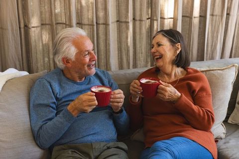 Happy senior couple enjoying coffee on cozy sofa at home