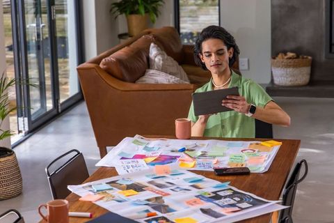 Asian creative reviewing moodboard and sticky notes at modern home workspace with tablet