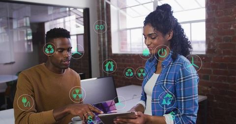 Collaborating on tablet with sustainability icons in modern office, teamwork renewable tech