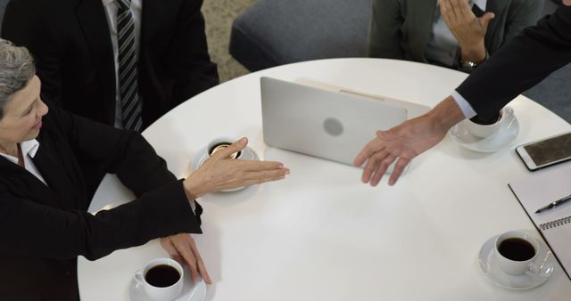 Business professionals shaking hands over coffee and laptops during a meeting. Ideal for themes related to corporate teamwork, business deals, meetings, and professional collaboration. Great for illustrating concepts of collaboration, networking, and successful business negotiations.