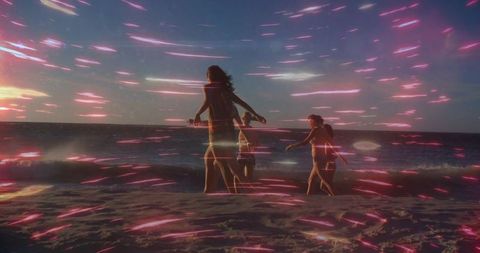 Walking along sunset beach with pink-purple light streaks and silhouetted friends