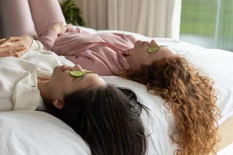 Diverse friends relaxing on bed with cucumber eye pads, cozy self-care and wellness moment