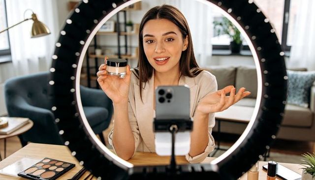 Beauty influencer filming makeup tutorial with led ring light and smartphone at home studio