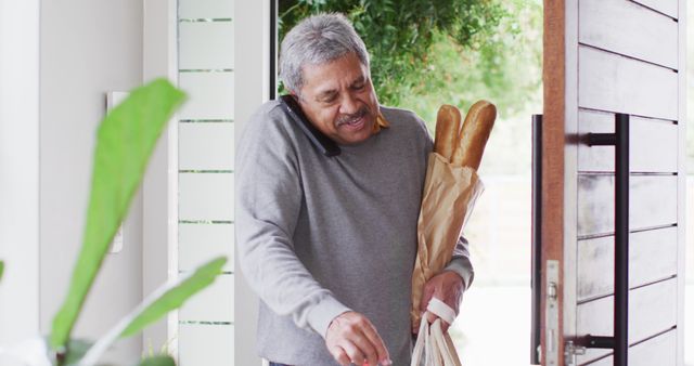 Man multitasking with phone and groceries in cozy home setting - Download Free Stock Images Pikwizard.com