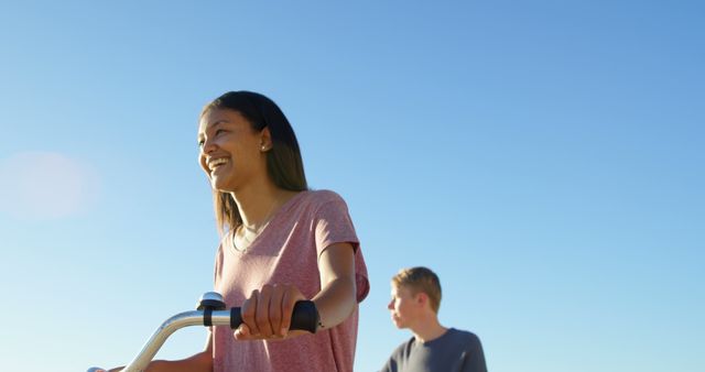 Smiling Young Woman and Friend Riding Bicycles Outdoors Under Blue Sky - Download Free Stock Images Pikwizard.com