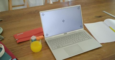 Working from home laptop on wooden desk with orange juice, coral case and notebook