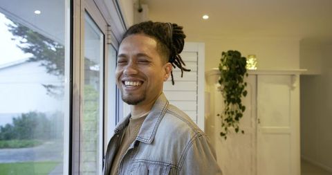 African american man standing by sliding door smiling in denim jacket, indoor lifestyle