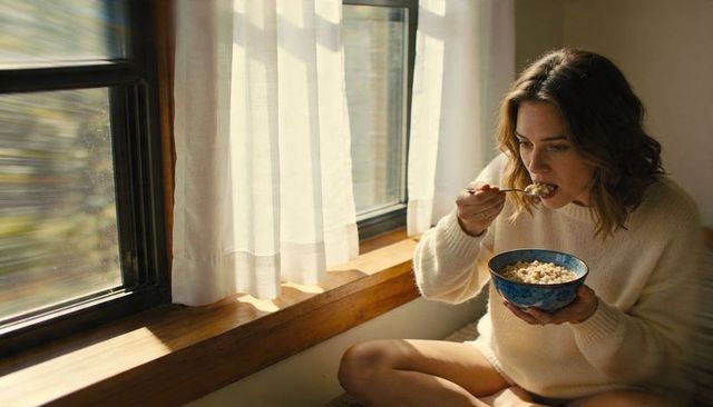 Cozy morning routine woman eating breakfast on window seat holding blue ceramic bowl