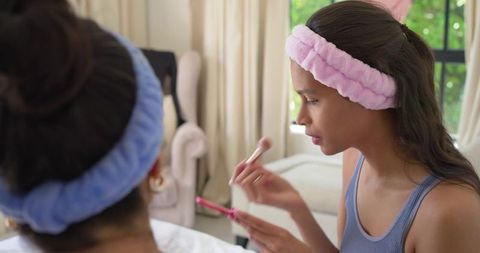 Teen and woman applying makeup together on bed wearing plush headbands skincare routine