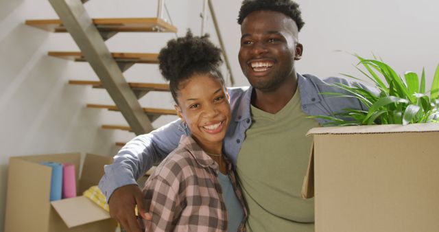 Young African American couple is excitedly moving into their new home. They are smiling and standing close to each other, showing happiness and anticipation for their new beginning. This image is perfect for themes related to homeowners, relocation services, positive relationships, and new life chapters. Ideal for use in real estate advertisements, moving company promotions, lifestyle blogs, and social media content emphasizing family life and home improvement.