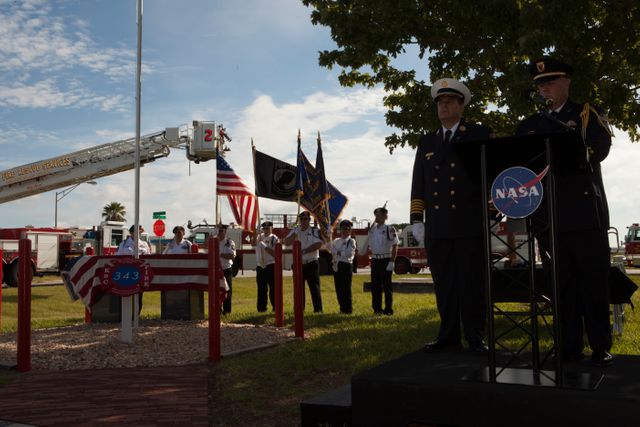 Rick Anderson, fire chief at NASA's Kennedy Space Center, on podium, left, and Lt. James Dumont lead the dedication service for a memorial to the343 first responder victims of the Sept. 11, 2001, terror attacks at Kennedy's Fire Station 1 on Sept. 11, 2015. The ceremony dedicated a monument that includes a section of steel I-beam from the World Trade Center in New York.