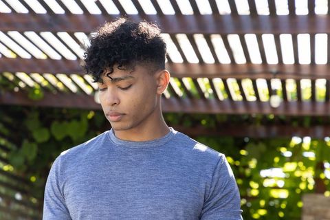African american man standing under pergola, looking down, contemplative garden portrait