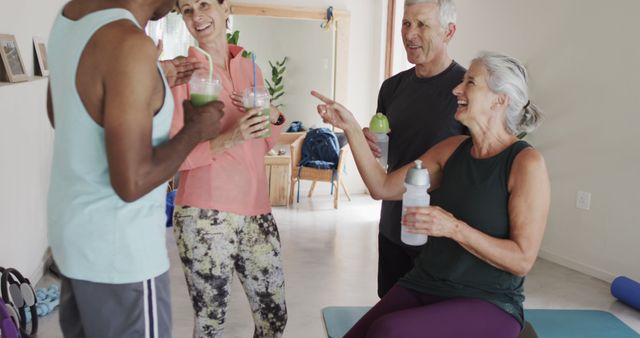 Group of senior friends laughing and chatting after an exercise session while holding refreshing smoothies. They appear to be inside a home gym or living room, emphasizing a healthy, active lifestyle and strong social connections among older adults. Suitable for promoting senior fitness classes, healthy lifestyle brands, or social activities for seniors.