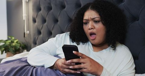 Midadult african american woman in bed reacting to shocking smartphone message at night