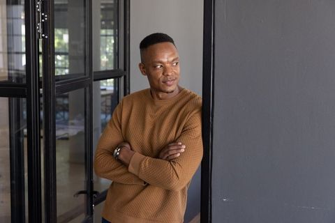 African American man leaning against glass doorframe checking smartwatch in modern office corridor