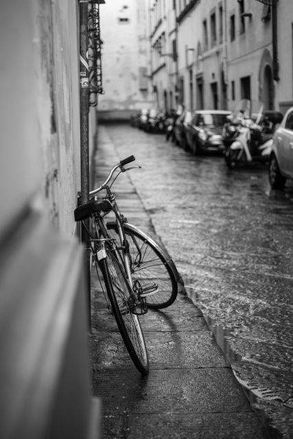 Classic black and white scene featuring a vintage bicycle leaning on an old wall in a narrow European alley. Ideal for use in travel brochures, historical articles, or urban lifestyle blogs. The wet pavement and cobblestone street evoke a nostalgic and tranquil atmosphere.