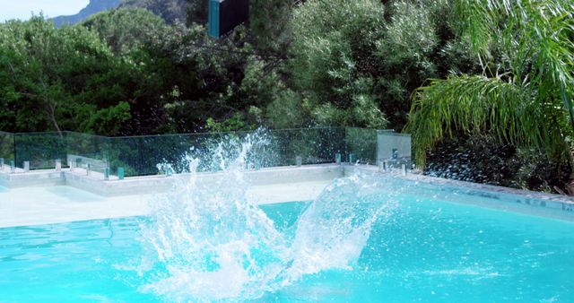 A bright and sunny day at a poolside where a kid has just jumped in, creating a large splash. The background is filled with lush green trees and foliage, indicating a vibrant, natural setting. This image can be used for summer vacation promotions, pool safety campaigns, or advertisements for swimwear and outdoor activities.