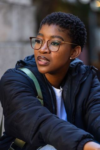 African woman wearing glasses and puffer jacket looking right, urban outdoor portrait, city vibe