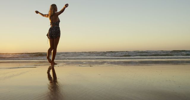 Woman standing on beach during sunset with arms spread, facing the ocean. Waves gently lap at her feet, creating a serene and tranquil atmosphere. Ideal for themes of relaxation, freedom, summer vacations, self-discovery, and escaping everyday life. Suitable for travel blogs, relaxation and wellness promotions, inspirational content, and advertisements for beach resorts.