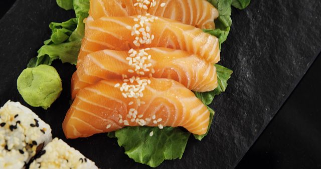 Freshly prepared salmon sashimi arranged on lettuce leaves, garnished with sesame seeds, and accompanied by wasabi and sushi rolls, perfect for websites and blogs focused on healthy eating, Japanese cuisine, and gourmet dining experiences.