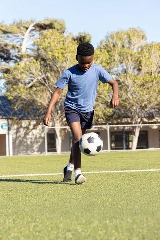 African american boy dribbling soccer ball on school field practicing youth football skills