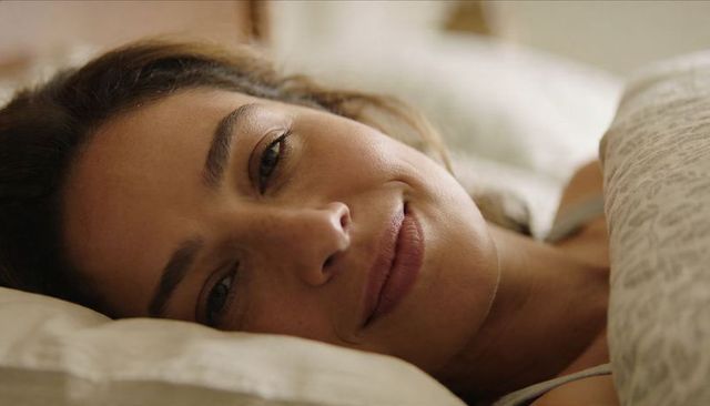 Serene woman smiling, resting on pillow with patterned duvet closeup in warm morning light
