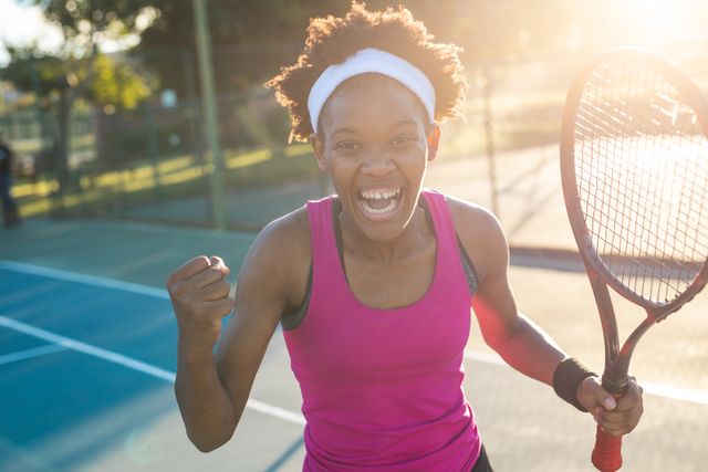 Portrait of happy african american female tennis player showing fist while cheering herself at court. unaltered, sport, competition and tennis game concept.