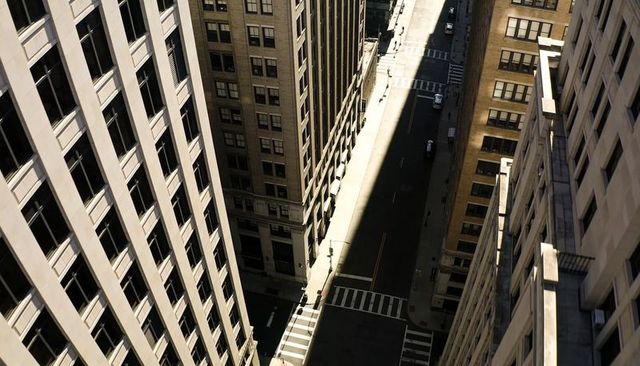 Sunlit urban canyon from above with narrow street, crosswalks and highrise shadows